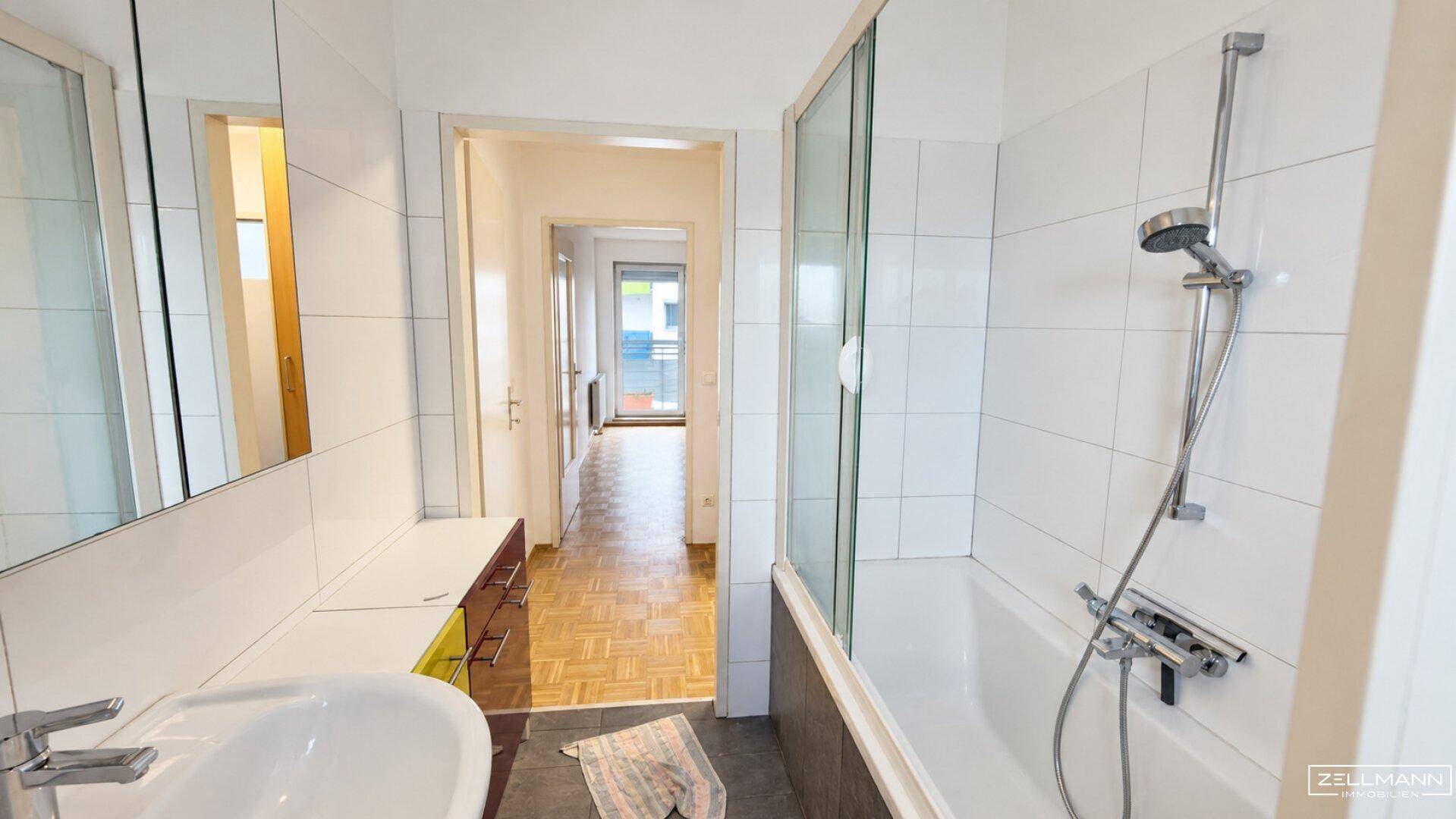 Helles Badezimmer mit Badewanne, Duschfunktion und einem Waschbecken mit Spiegelschrank.