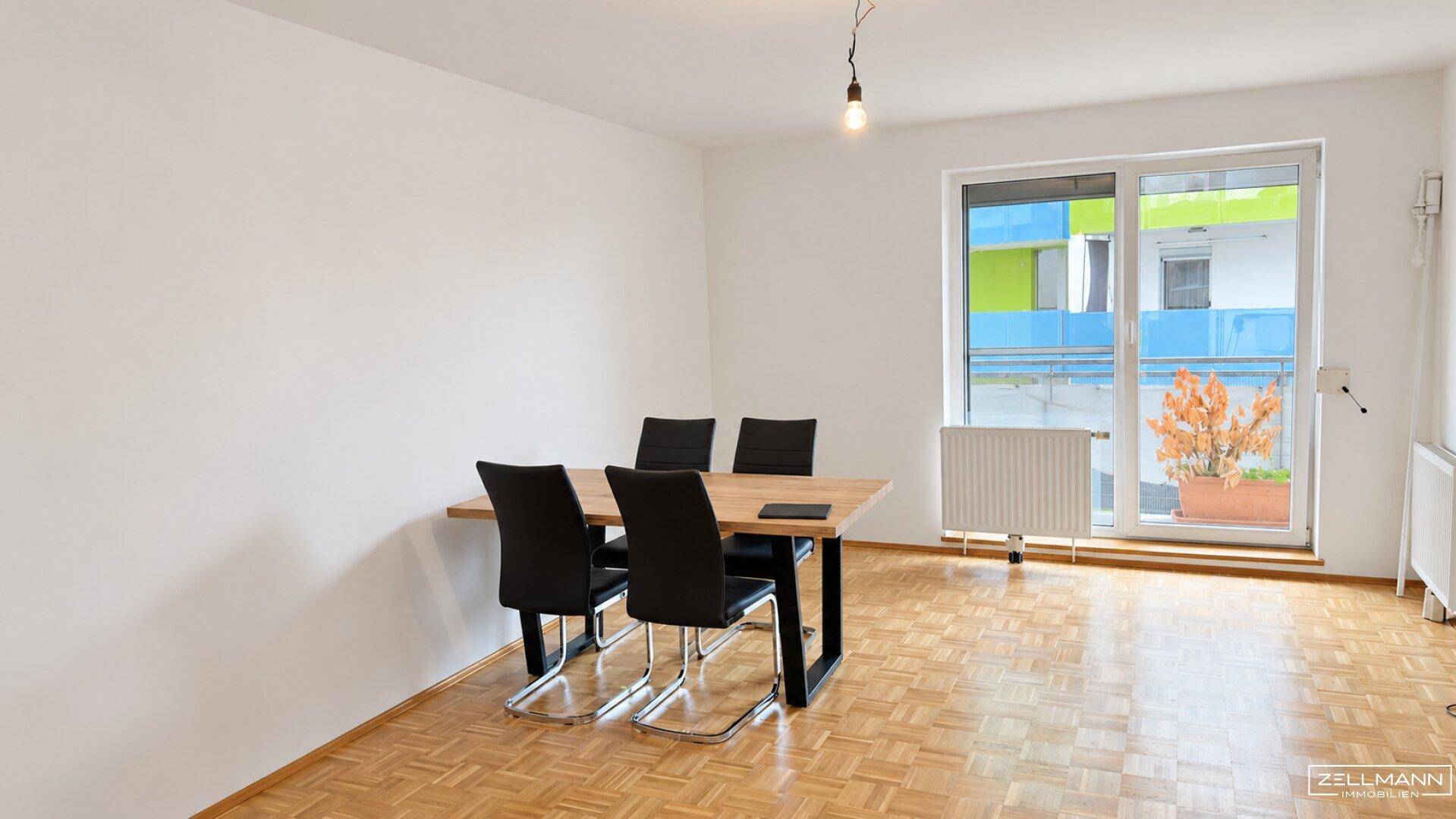 Geräumiger Wohn- und Essbereich mit Parkettboden, Esstisch und Zugang zum Balkon.