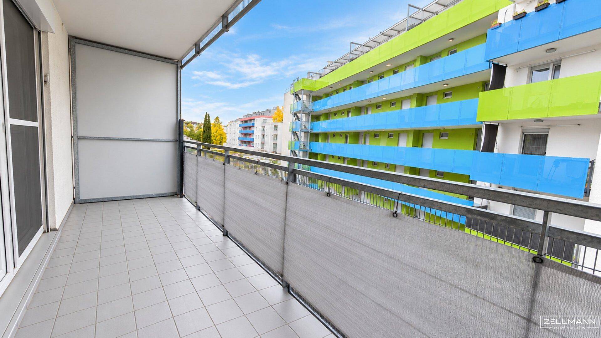 Geräumiger Balkon mit Fliesenboden und Blick auf die farbenfrohe Gebäudefassade.