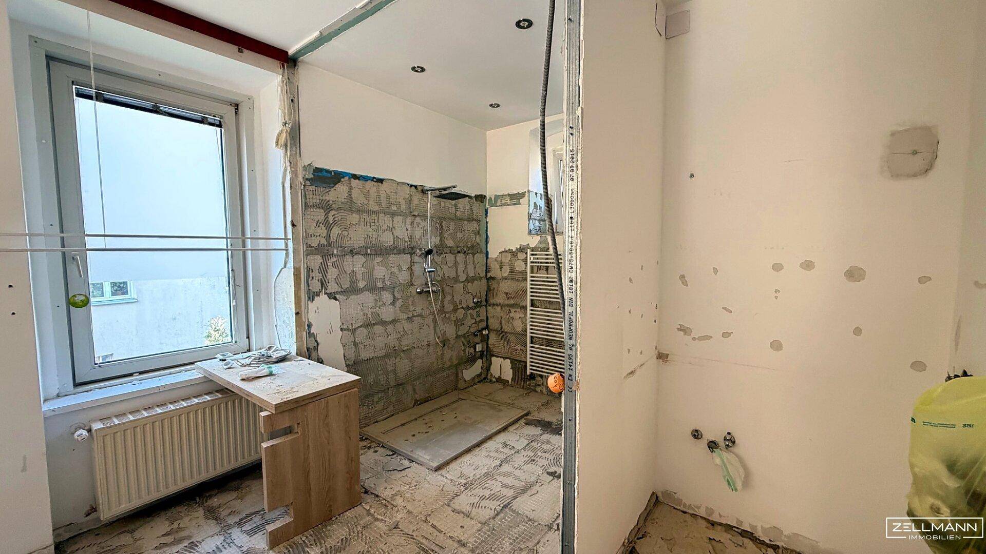 Badezimmer im Rohbau mit Fenster und Heizkörper, bereit für die Installation der Sanitärobjekte.