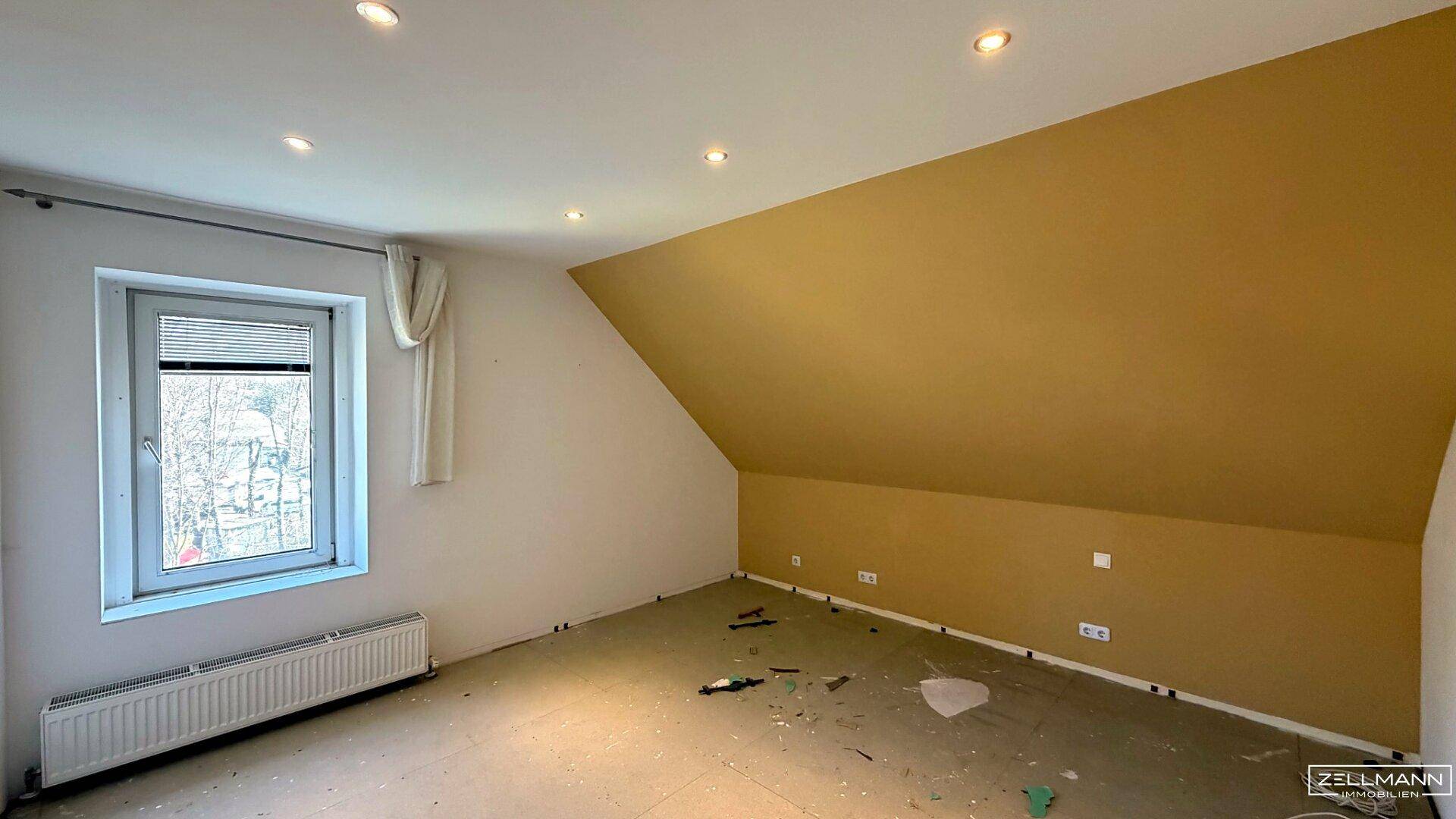 Dachgeschosszimmer mit schräger Wand, Einbaustrahlern und einem Fenster, bereit für die Gestaltung.