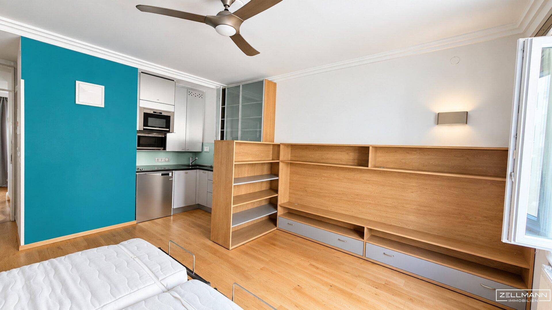 Geräumiger Wohnbereich mit Holzboden, integrierter Küchenzeile und Deckenventilator.