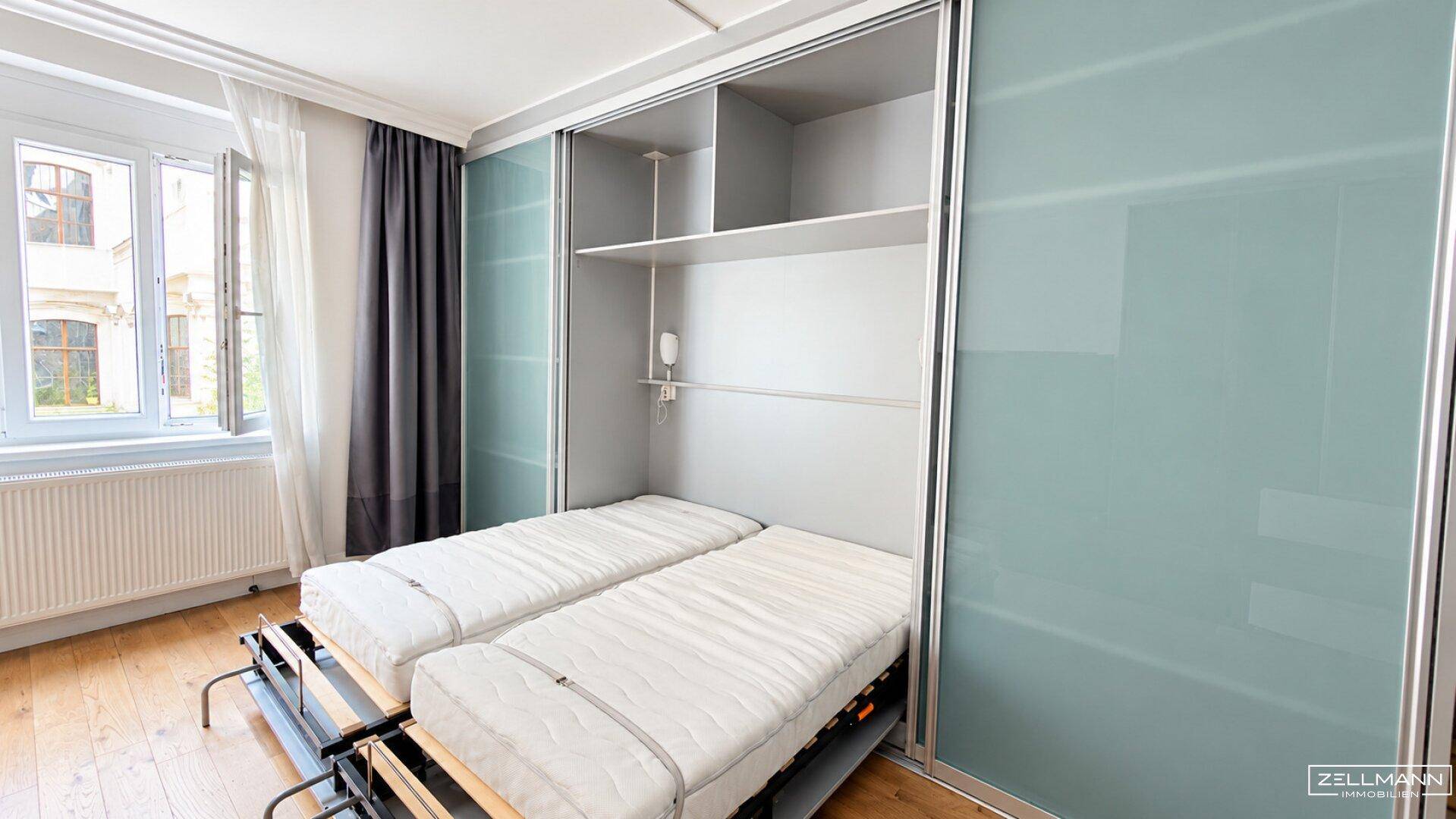 Schlafbereich mit integriertem Schrankbett, Holzboden und großem Fenster.