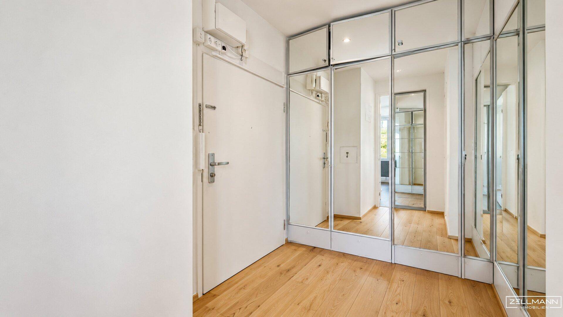 Eingangsbereich mit hellem Holzboden und raumhohen Spiegelschränken für viel Stauraum.