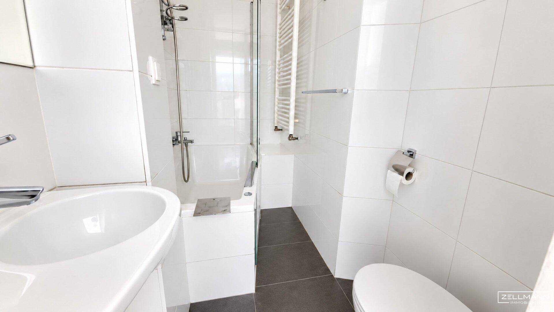 Modernes Badezimmer mit weißen Fliesen, Dusche und beheiztem Handtuchhalter.