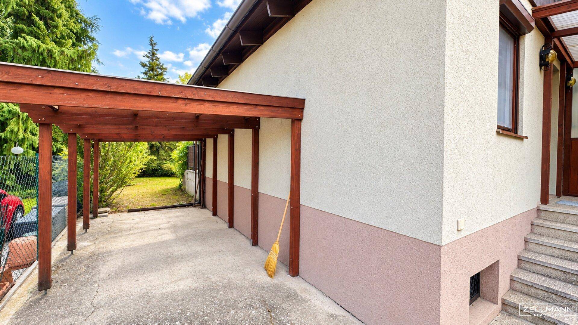 Seitenansicht des Hauses mit überdachtem Carport und Zugang zum Eingangsbereich über eine Steintreppe.