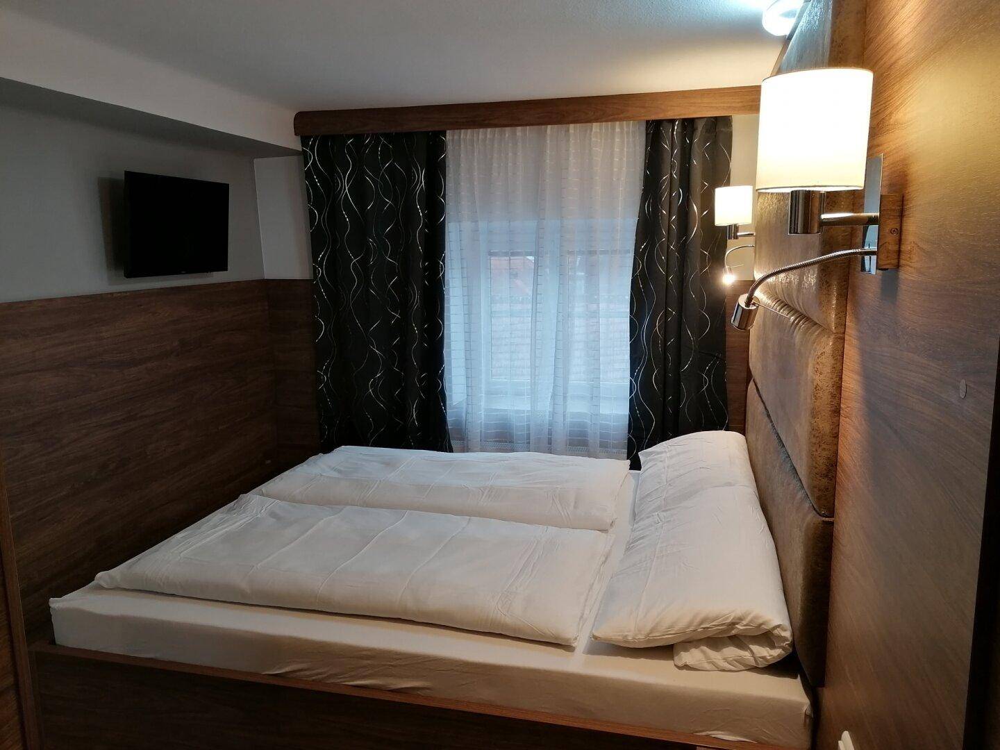 Gemütliches Schlafzimmer mit Doppelbett, Holzvertäfelung und dunklen Vorhängen am Fenster.