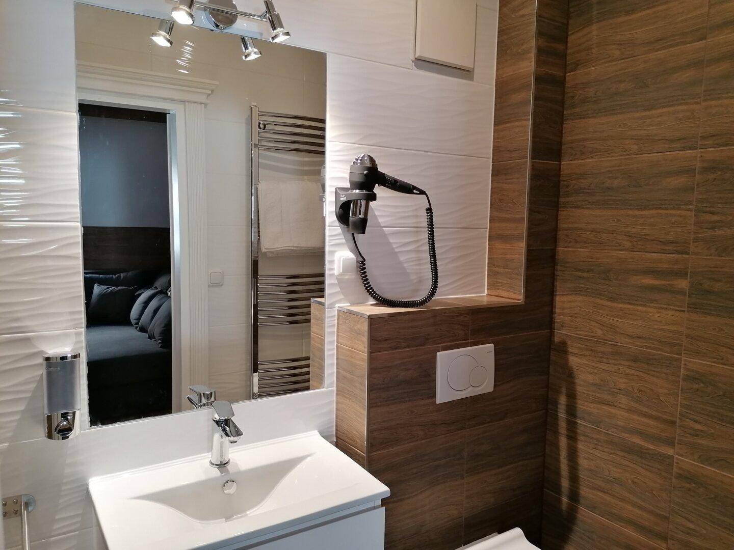 Badezimmer mit Waschtisch, Spiegel und Föhn, daneben ein Handtuchheizkörper.