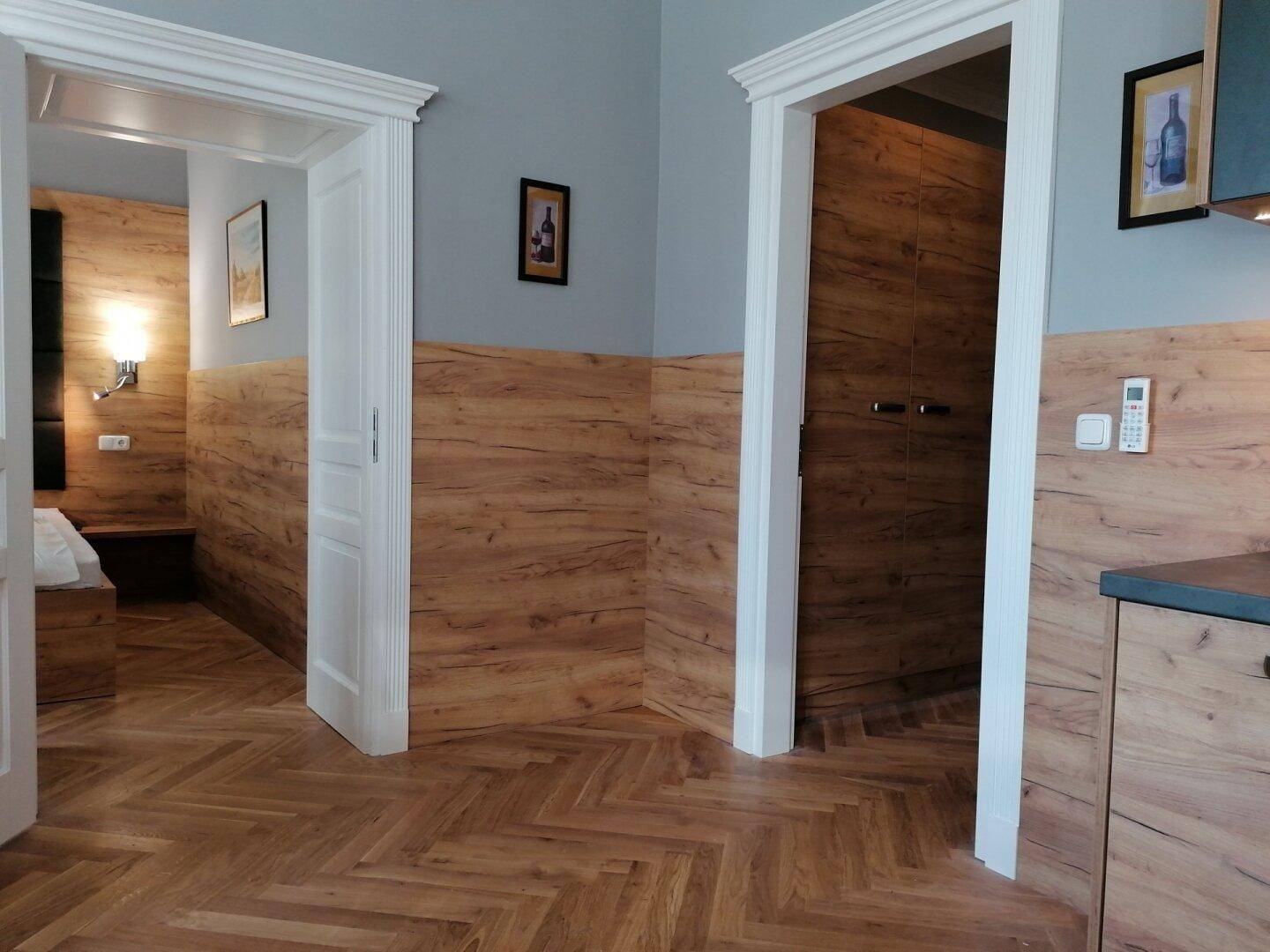 Offener Wohnbereich mit Holzboden, zwei Türen und Holzvertäfelung an den Wänden.