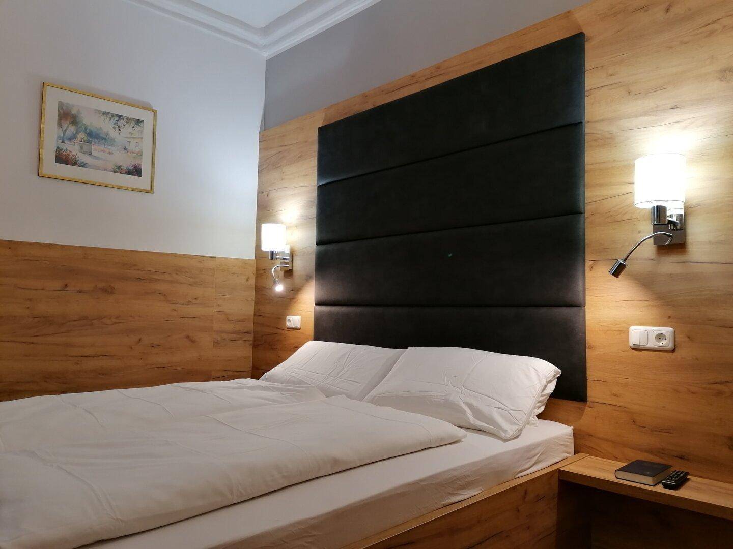 Schlafzimmer mit Doppelbett, gepolstertem Kopfteil und Holzvertäfelung an der Wand.