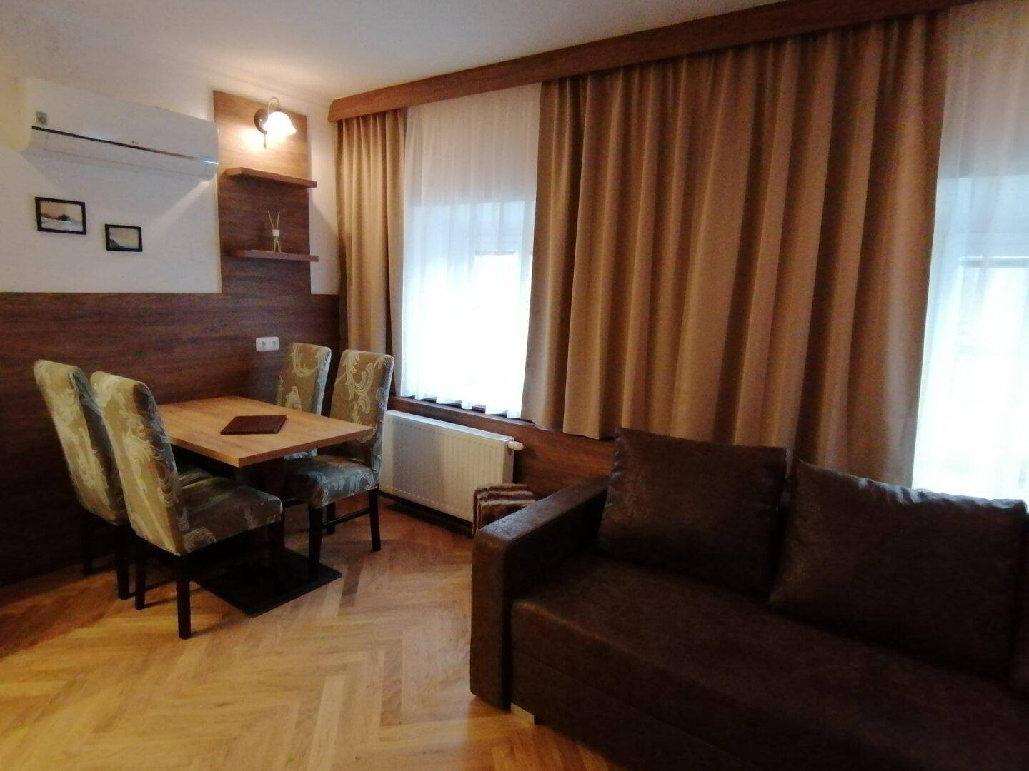 Wohn- und Essbereich mit Sofa, Esstisch und großen Fenstern mit Vorhängen.