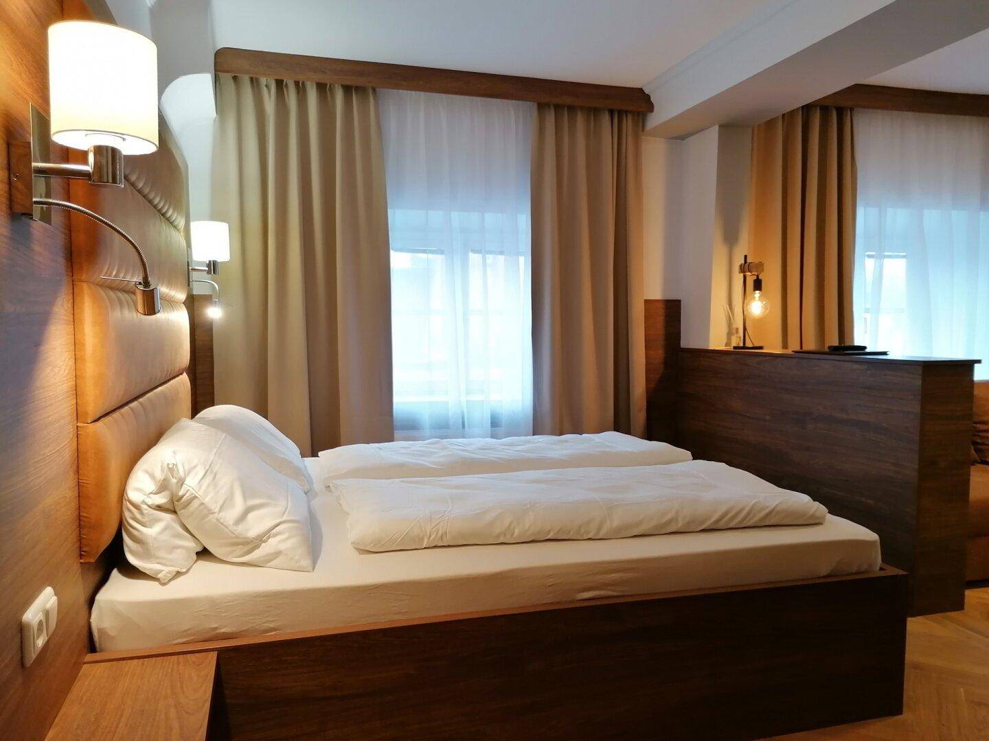 Schlafzimmer mit Doppelbett, Holzvertäfelung und großen Fenstern mit Vorhängen.