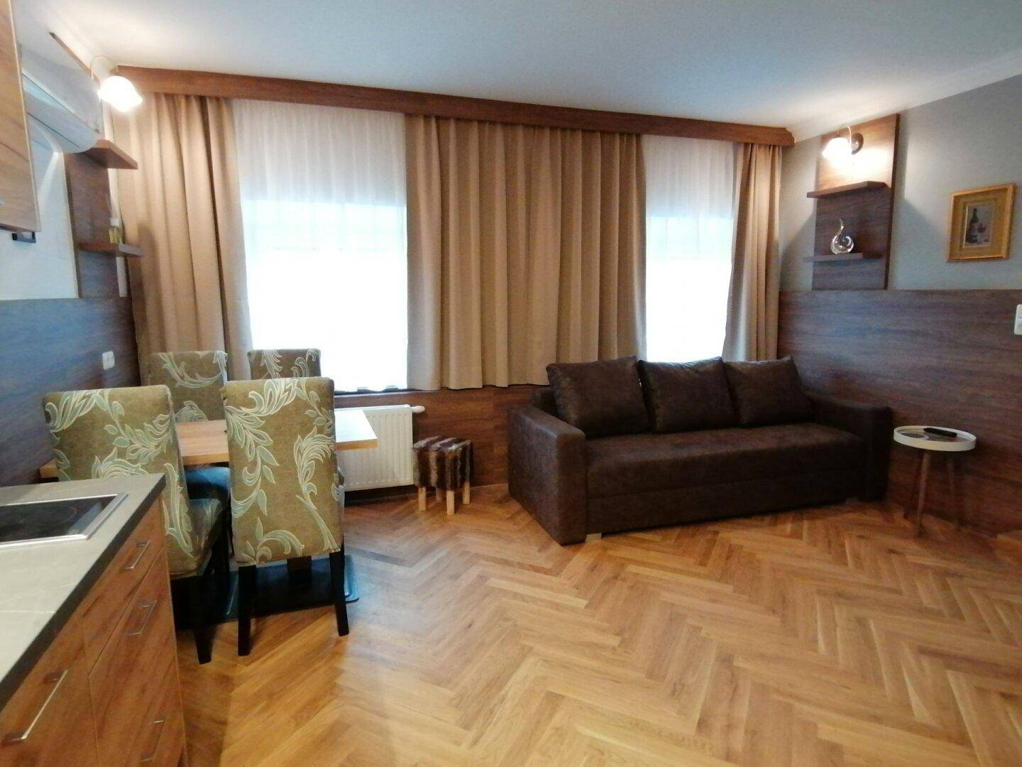Wohn- und Essbereich mit Sofa, Esstisch und integrierter Küchenzeile im Hintergrund.
