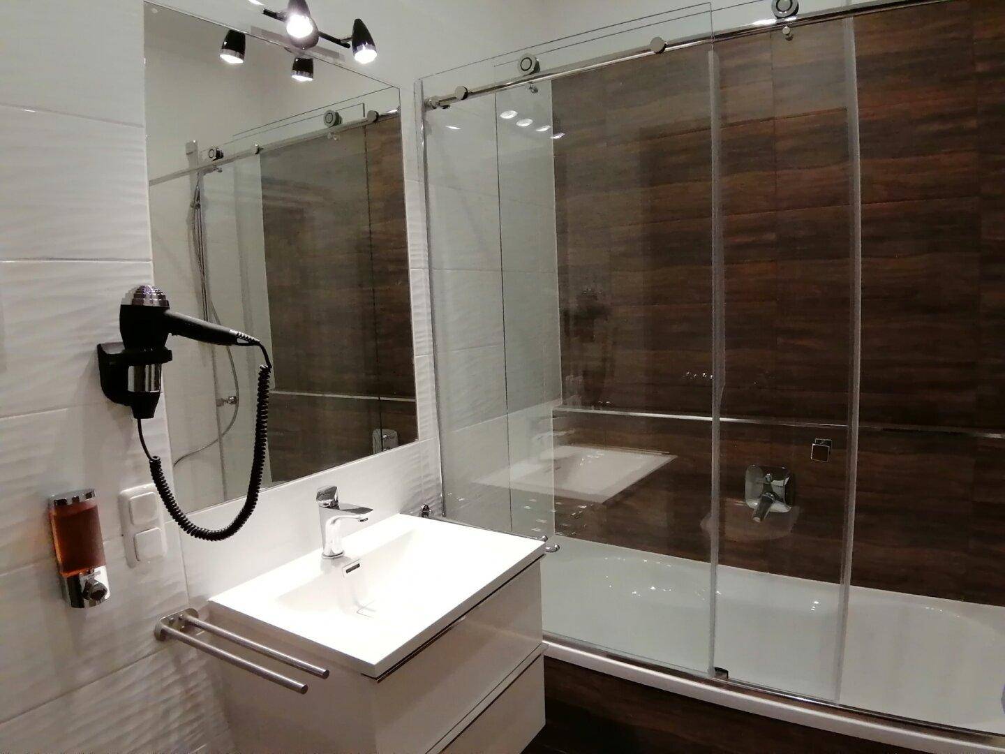 Modernes Badezimmer mit Waschtisch, Spiegel und Duschbadewanne mit Glasschiebetür.