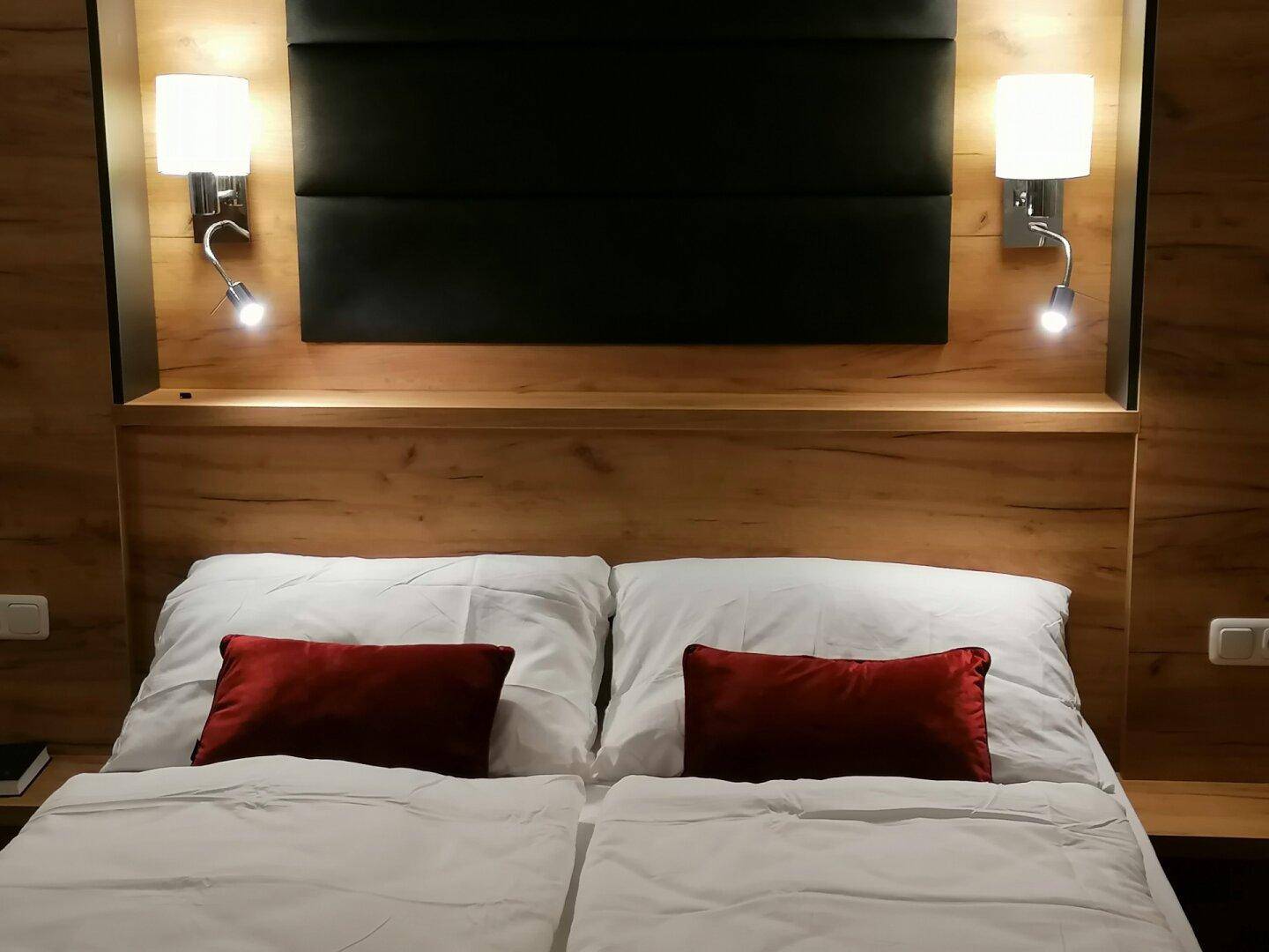 Schlafzimmer mit Doppelbett, gepolstertem Kopfteil und roten Kissen als Akzent.