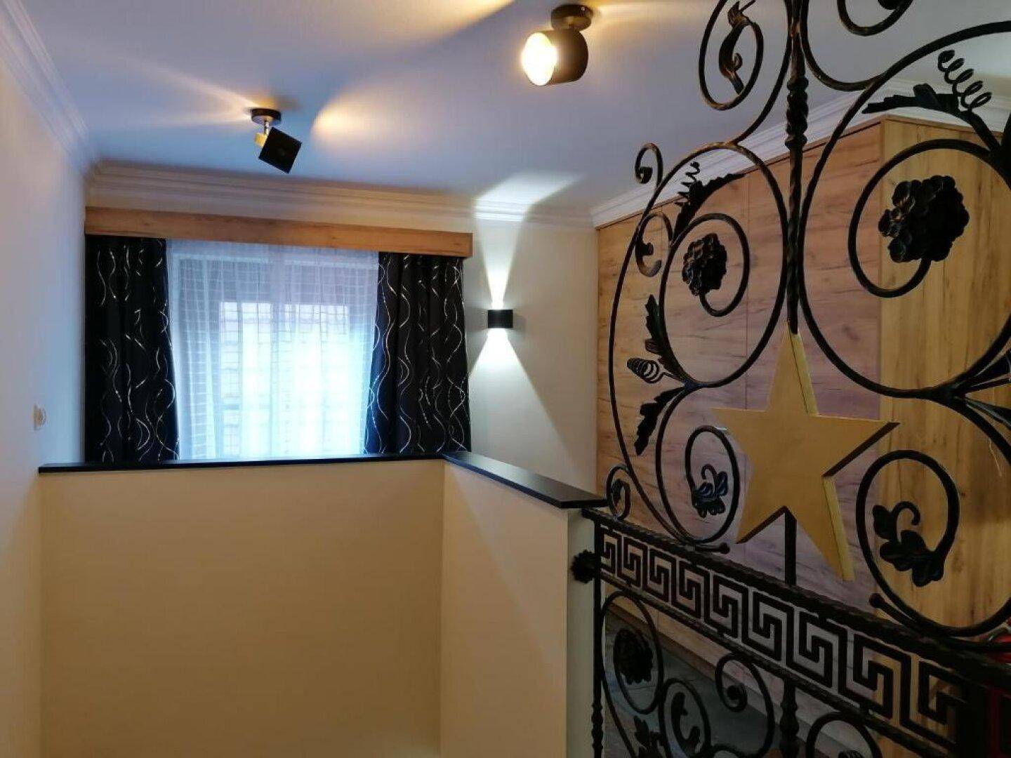Treppenabsatz mit kunstvollem schmiedeeisernem Geländer, Fenster und Holzverkleidung an der Wand.