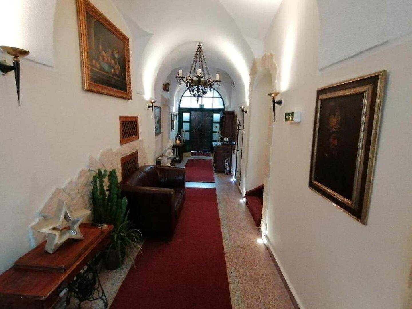 Langer Flur mit Gewölbedecke, rotem Teppichläufer, antiken Möbeln und klassischen Gemälden an den Wänden.