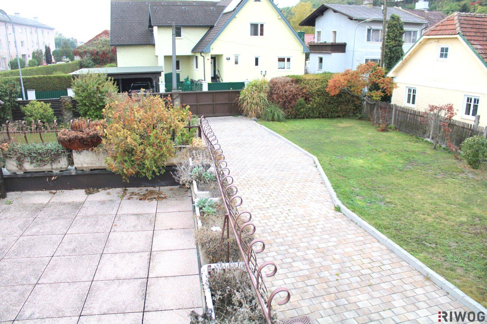 Erhöhter Blick auf die gepflasterte Auffahrt und den gepflegten Gartenbereich des Anwesens mit umliegenden Häusern.