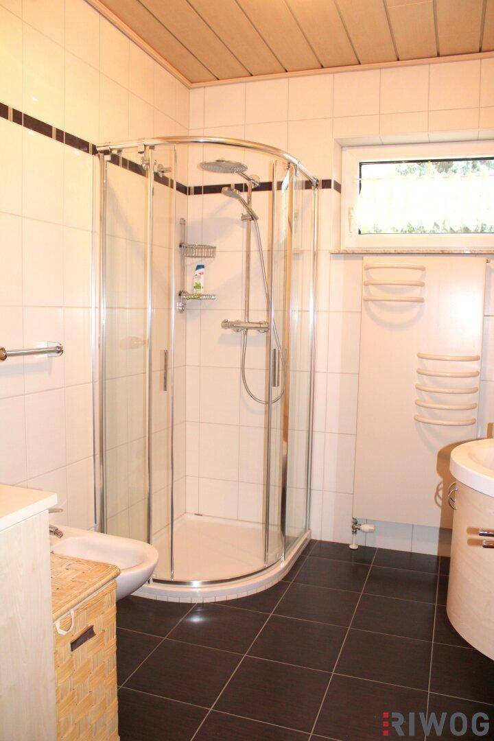 Badezimmer mit Eckdusche, Bidet, Handtuchheizkörper, Fenster und gefliesten Wänden und Boden.