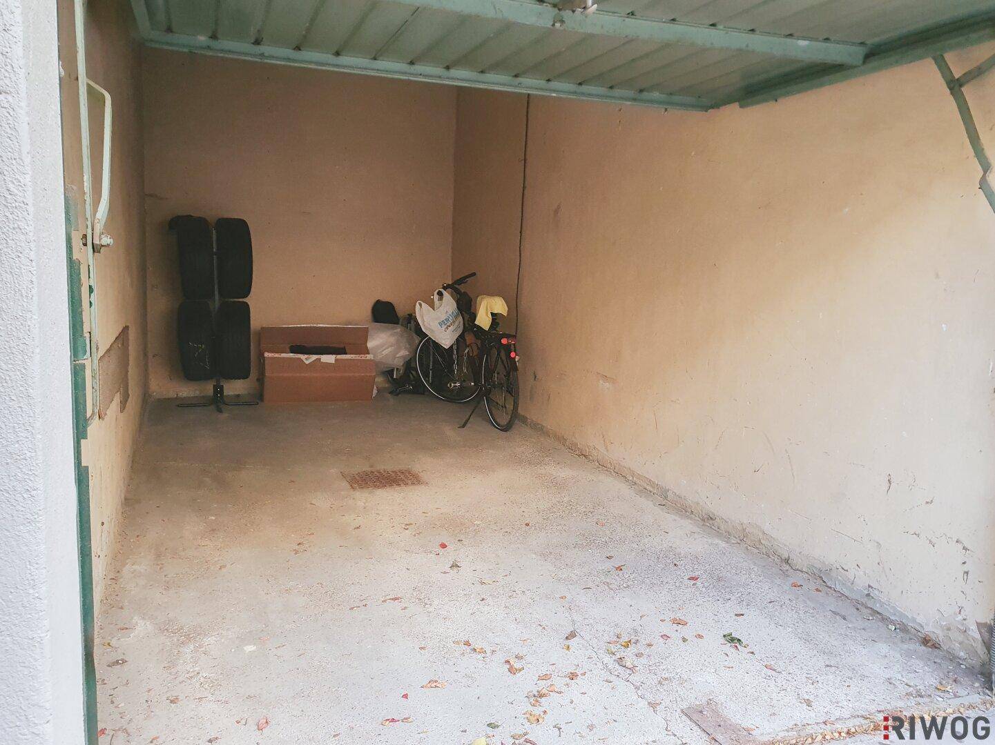 Leere Einzelgarage mit Betonboden, in der Reifen und ein Fahrrad an der Rückwand gelagert sind.