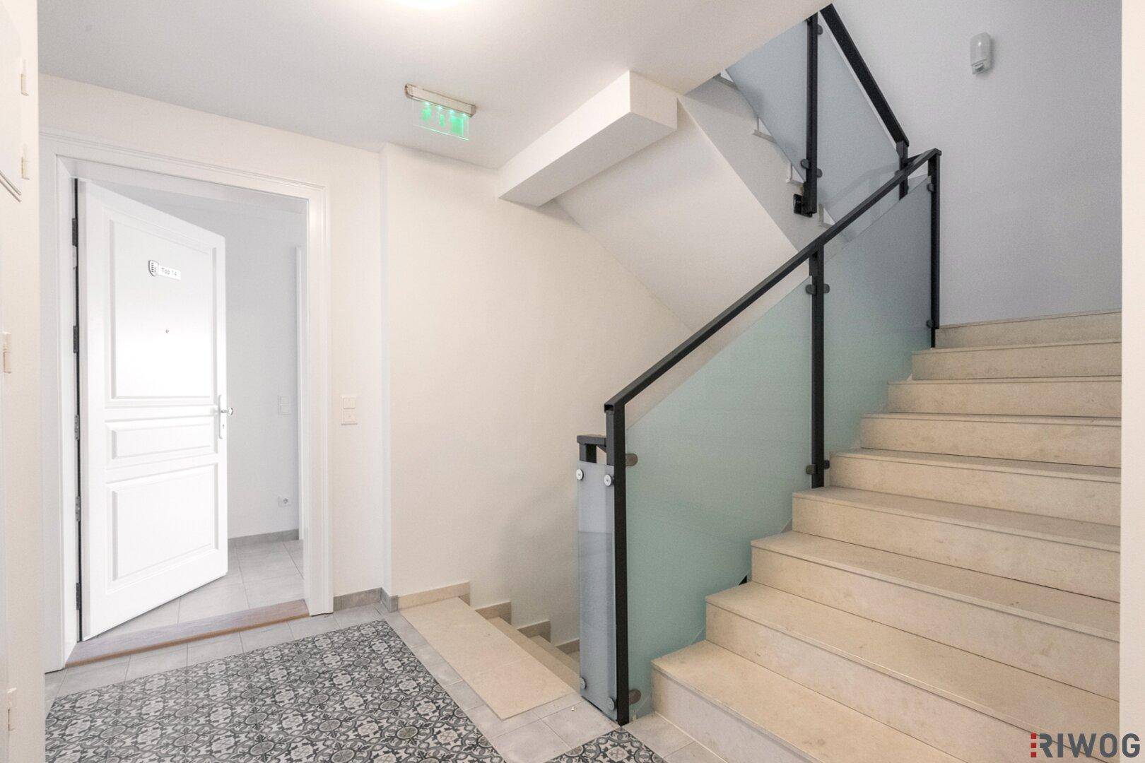 Modernes Treppenhaus mit Glasgeländer und hellem Steinboden, führt zu den oberen Etagen.
