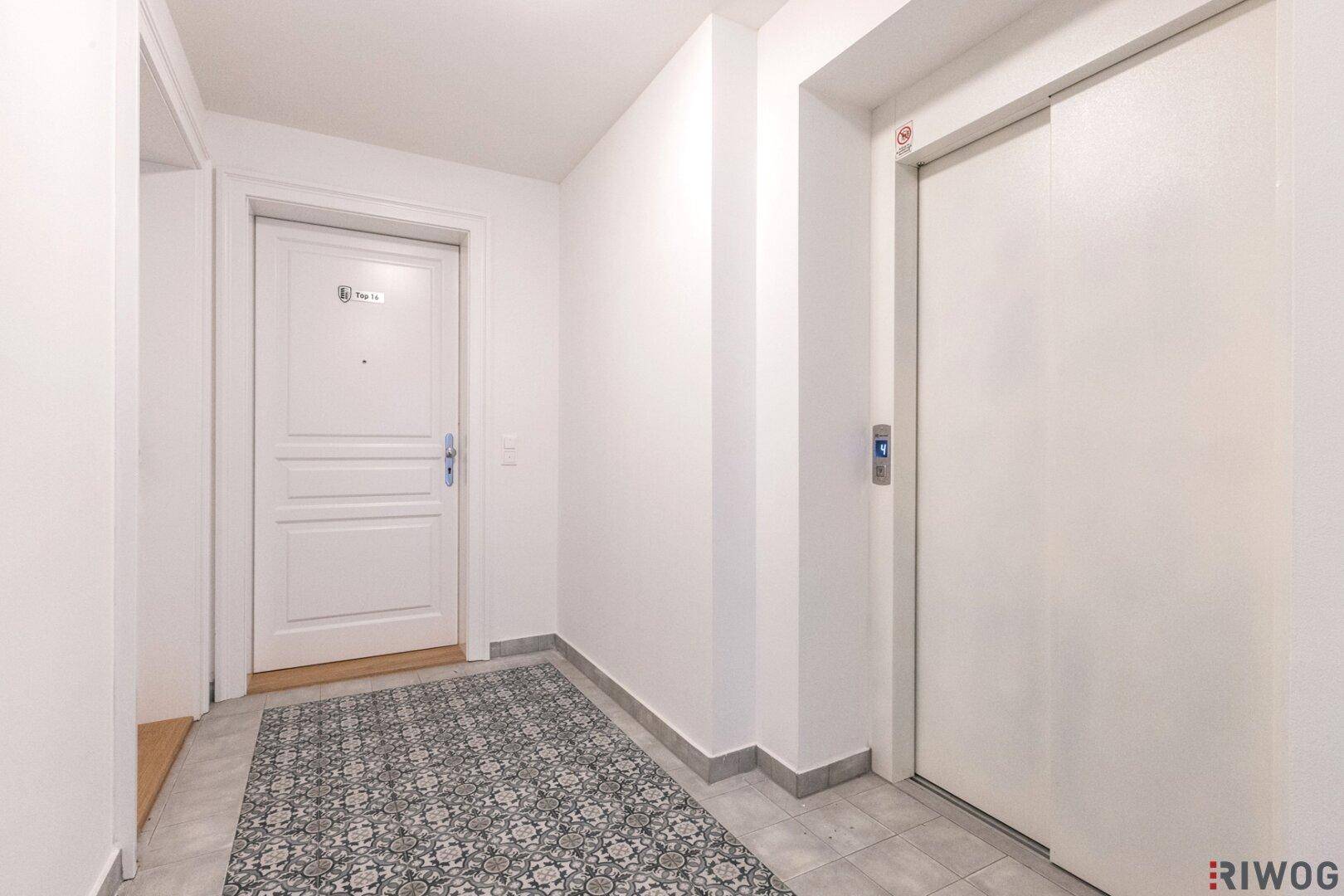Eingangsbereich mit Aufzug und Zugang zu einer Wohnung, ausgestattet mit einem gemusterten Fliesenboden.