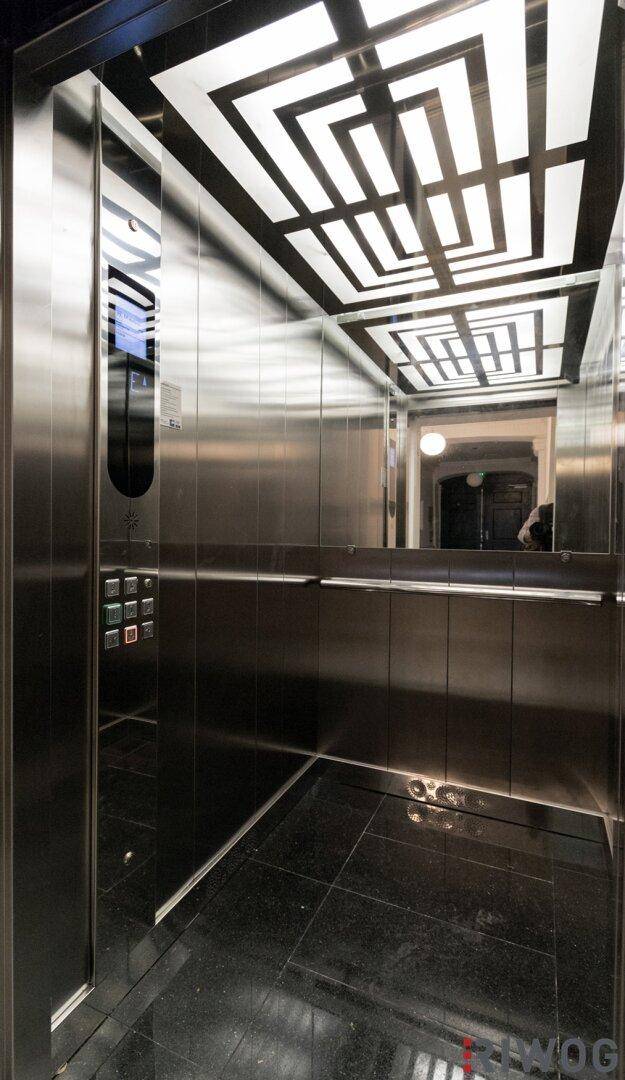 Moderne Aufzugskabine mit spiegelnden Metallwänden und einem auffälligen Deckenmuster.