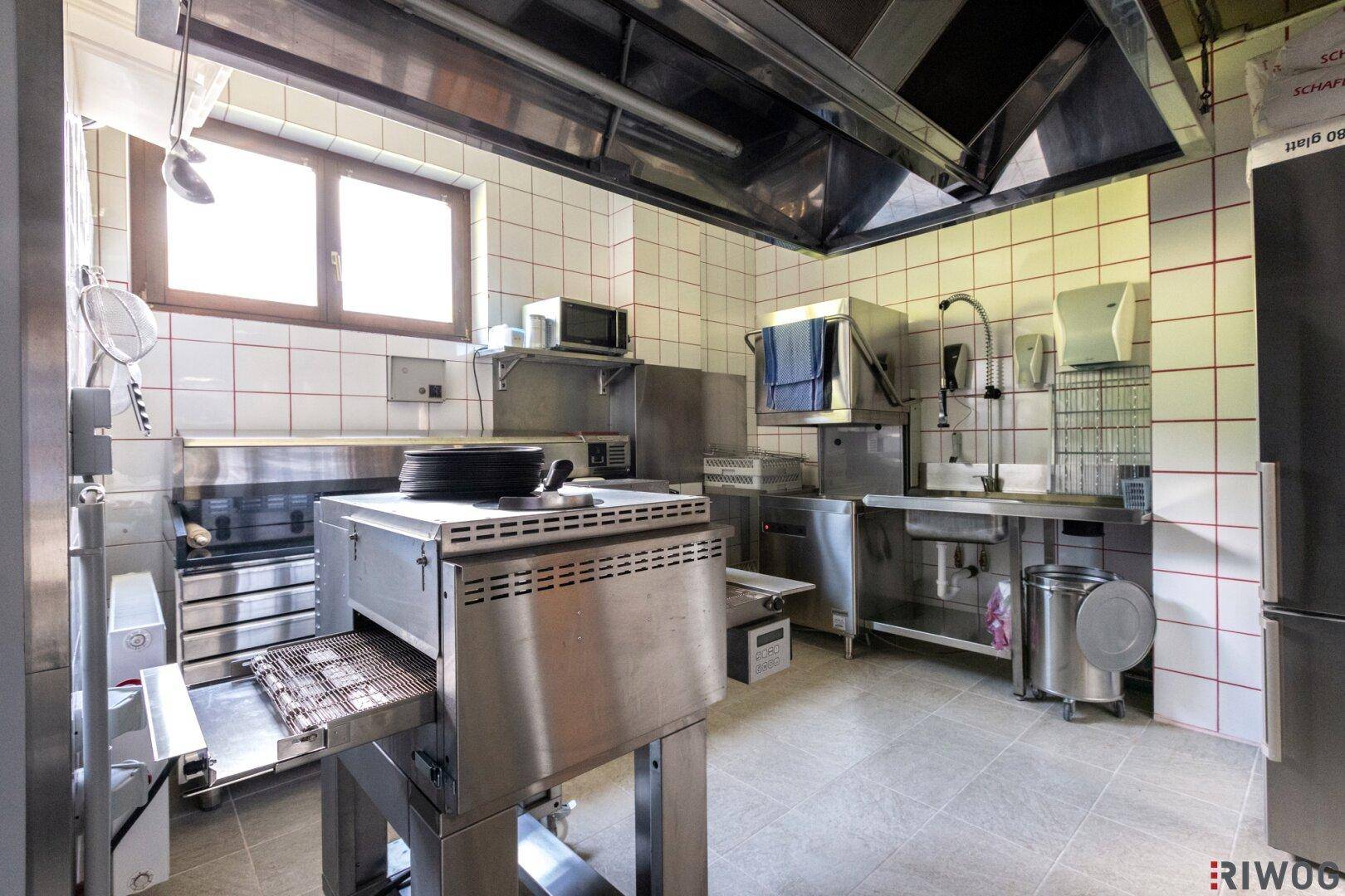 Professionelle Großküche mit Edelstahloberflächen, Fliesenwänden und industriellen Geräten.