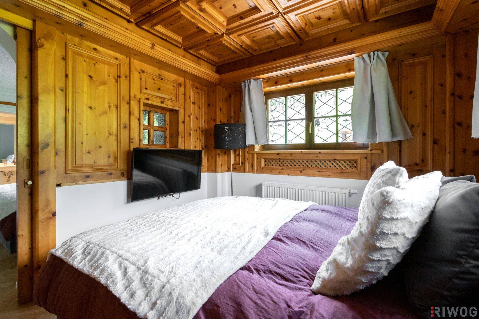 Gemütliches Schlafzimmer mit Holztäfelung, Kassettendecke und einem Fernseher an der Wand.