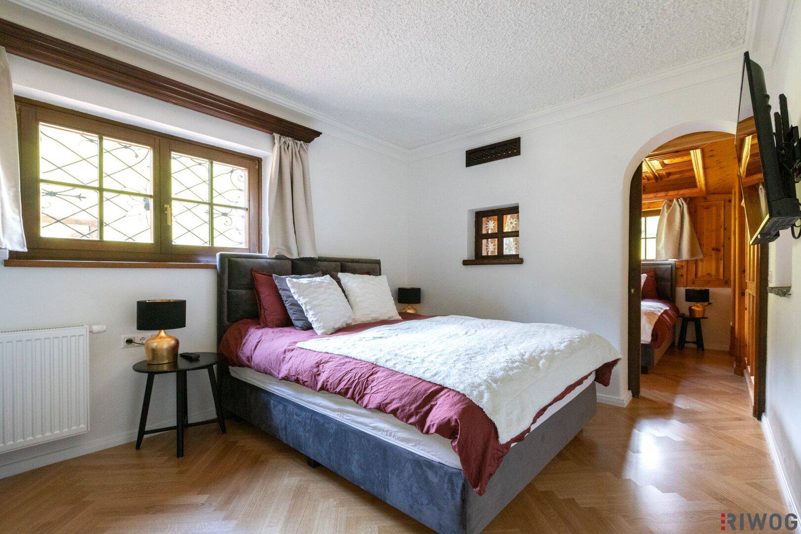 Schlafzimmer mit hellem Interieur, Holzboden und Blick auf einen angrenzenden Raum mit Holztäfelung.