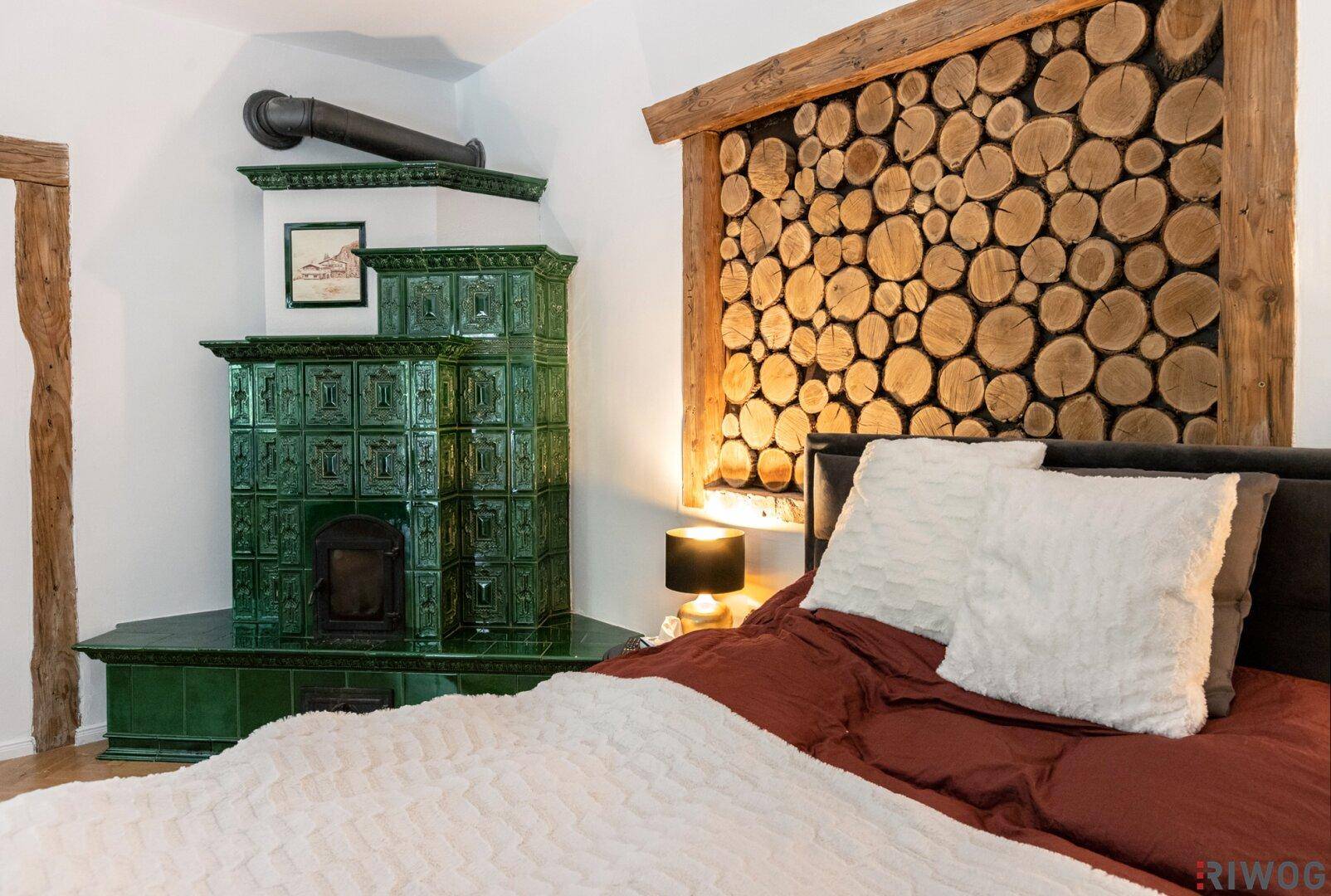 Schlafzimmer mit traditionellem Kachelofen und einer dekorativen Holzwand hinter dem Bett.