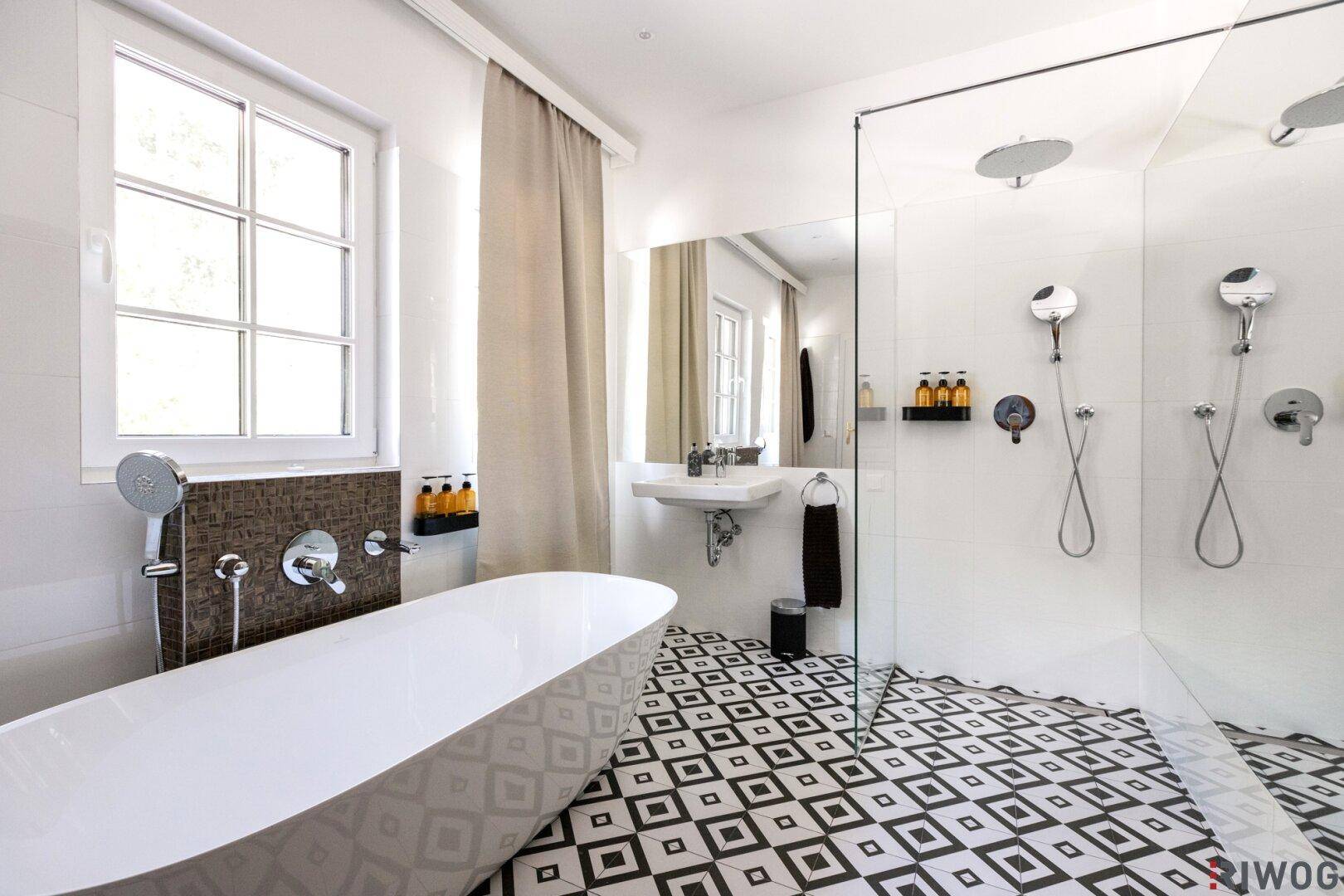 Modernes Badezimmer mit freistehender Badewanne, großer Dusche und auffälligen schwarz-weißen Fliesen.