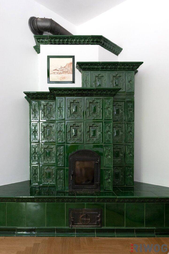 Detailaufnahme eines traditionellen grünen Kachelofens mit kunstvollen Verzierungen und Ofenrohr.