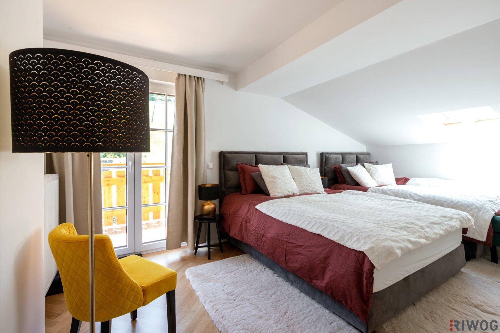 Dachgeschoss-Schlafzimmer mit schrägen Wänden, zwei Betten und Zugang zu einem Balkon.