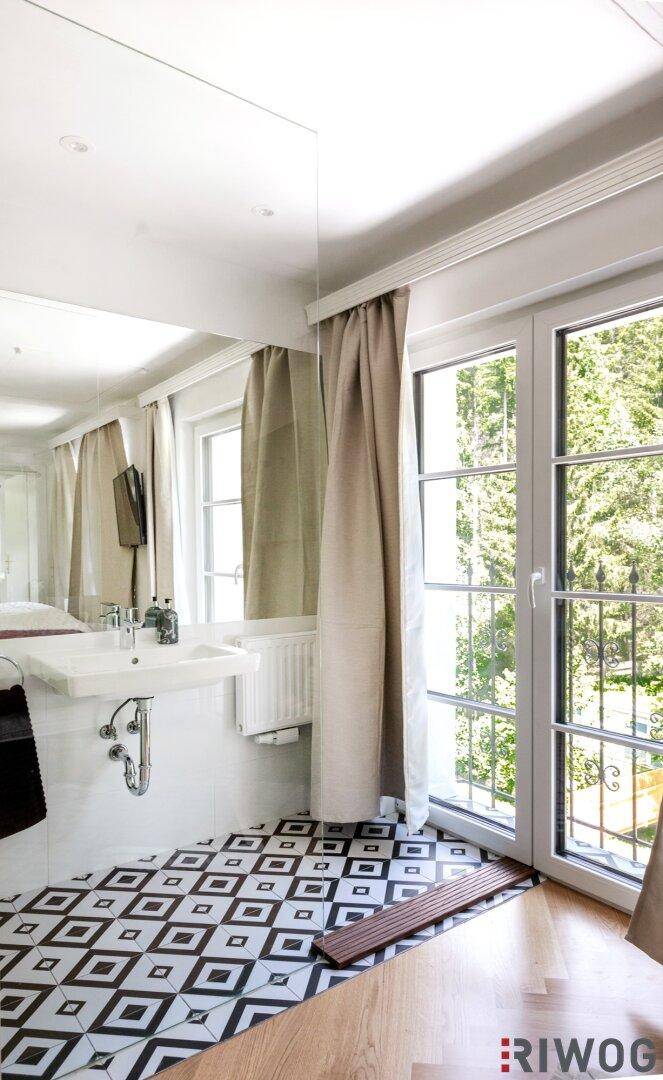Helles Badezimmer mit großem Fenster, Holzboden und einem Waschbecken mit Spiegel.