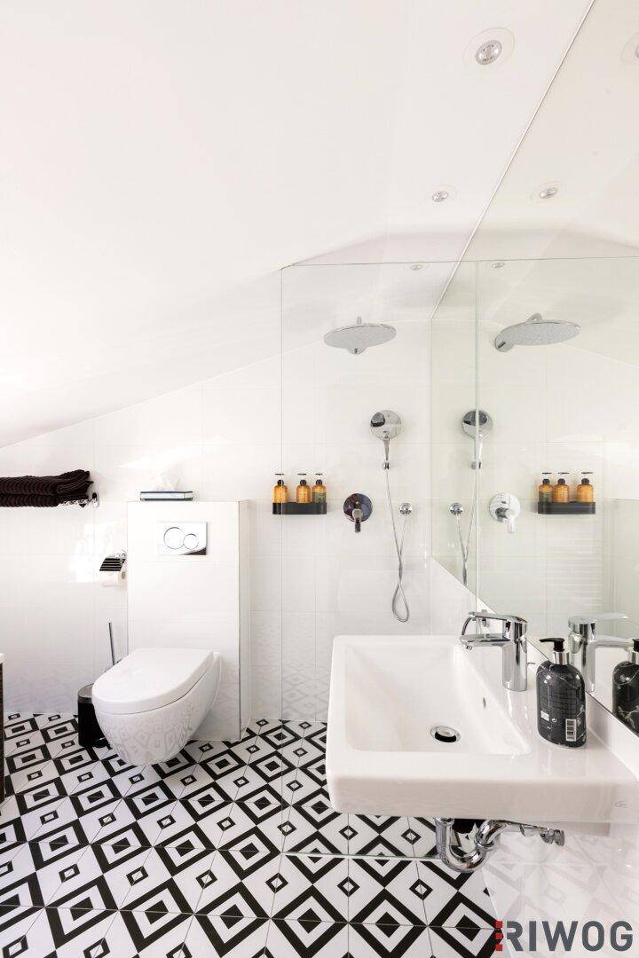 Helles Badezimmer mit Wand-WC, Waschbecken und großer Dusche unter einer Dachschräge.