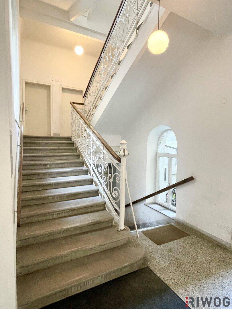 Elegantes Treppenhaus mit schmiedeeisernem Geländer und hohen Bogenfenstern.