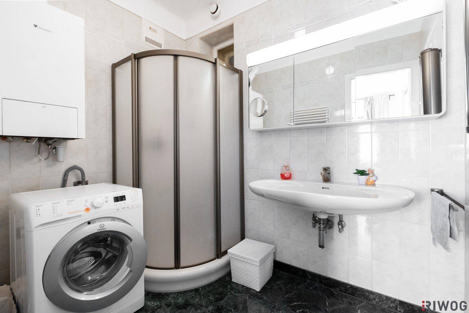 Badezimmer mit Duschkabine, Waschbecken, Spiegelschrank und integrierter Waschmaschine.