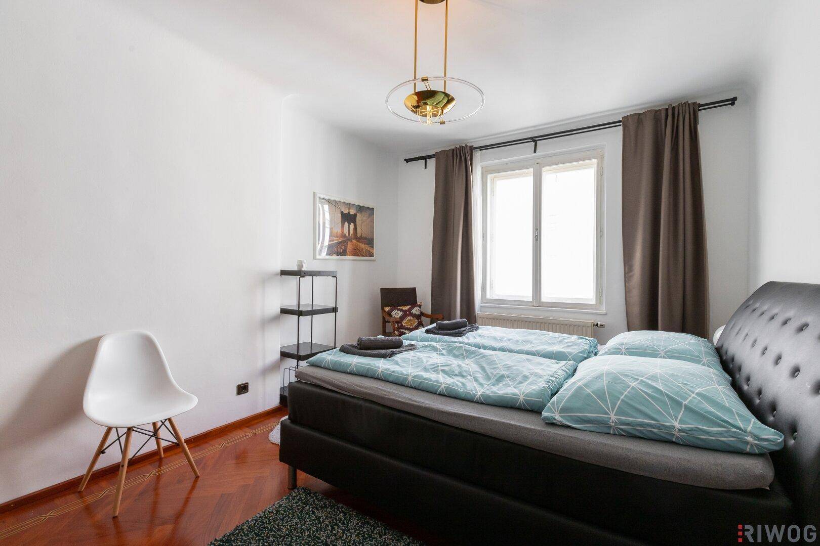 Gemütliches Schlafzimmer mit Doppelbett, Nachttisch und Fenster mit braunen Vorhängen.
