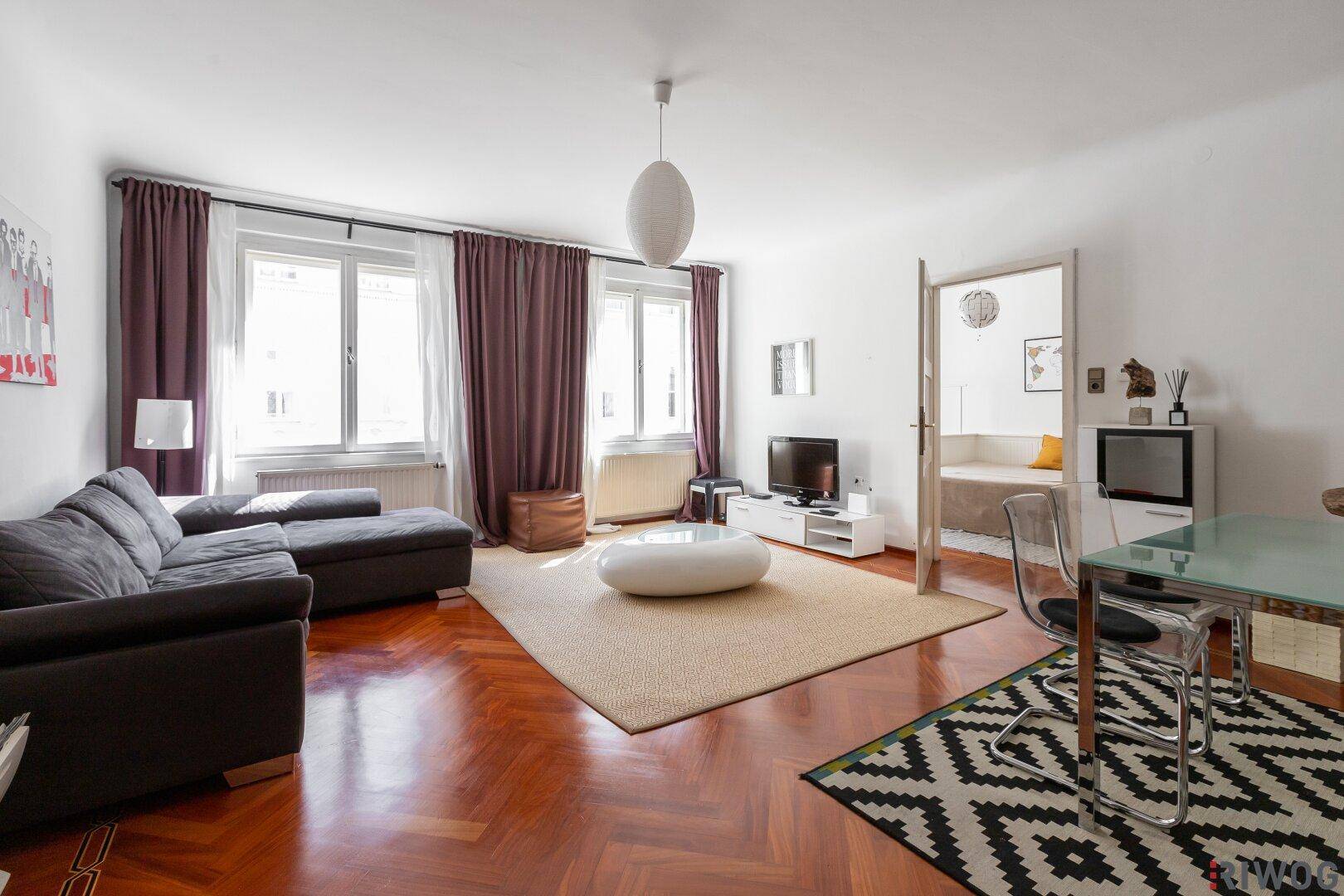 Geräumiger offener Wohn-Essbereich mit dunklem Sofa, Esstisch und elegantem Parkettboden.