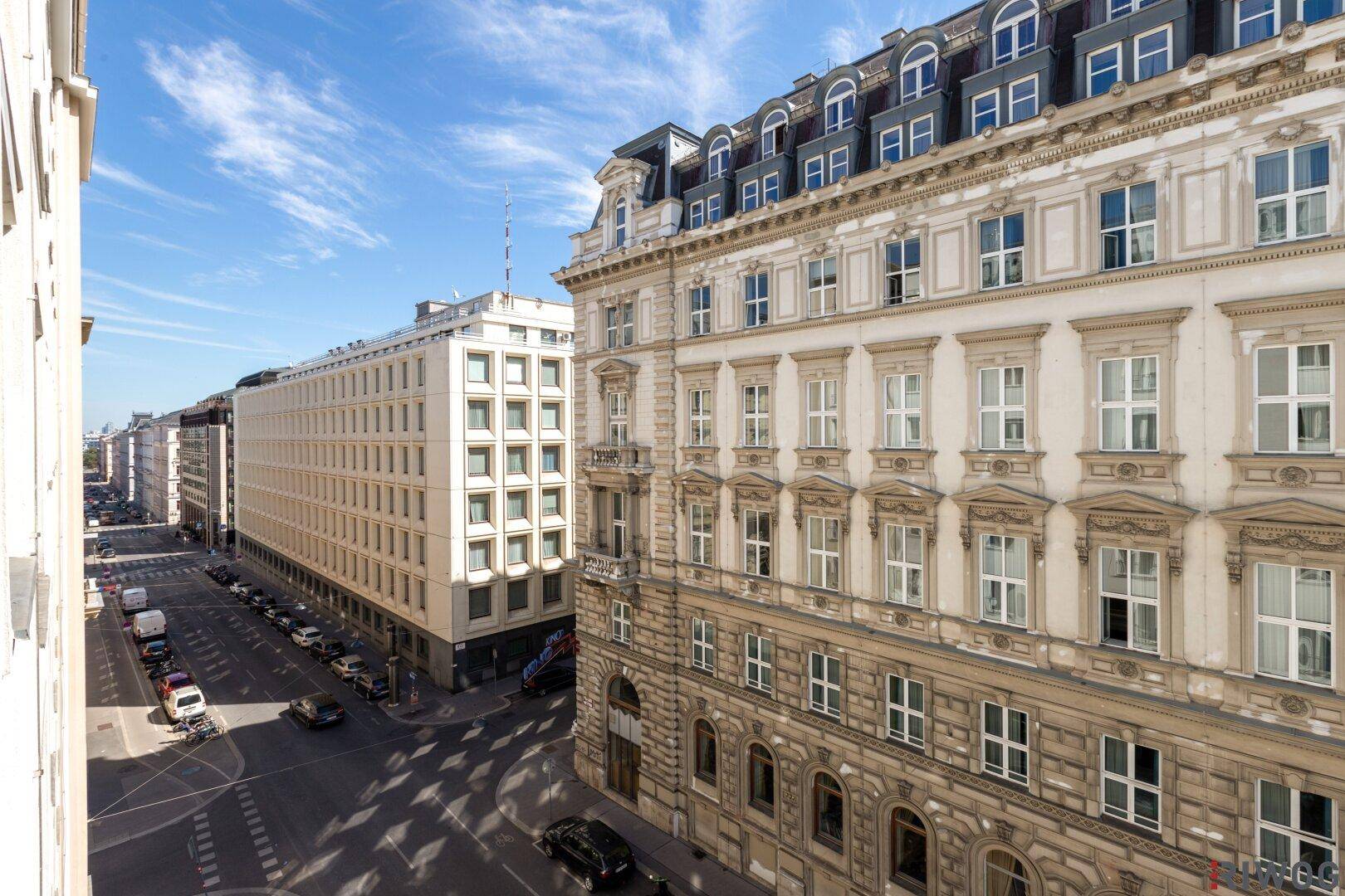 Blick von oben auf eine belebte Stadtstraße mit historischen und modernen Gebäuden unter blauem Himmel.