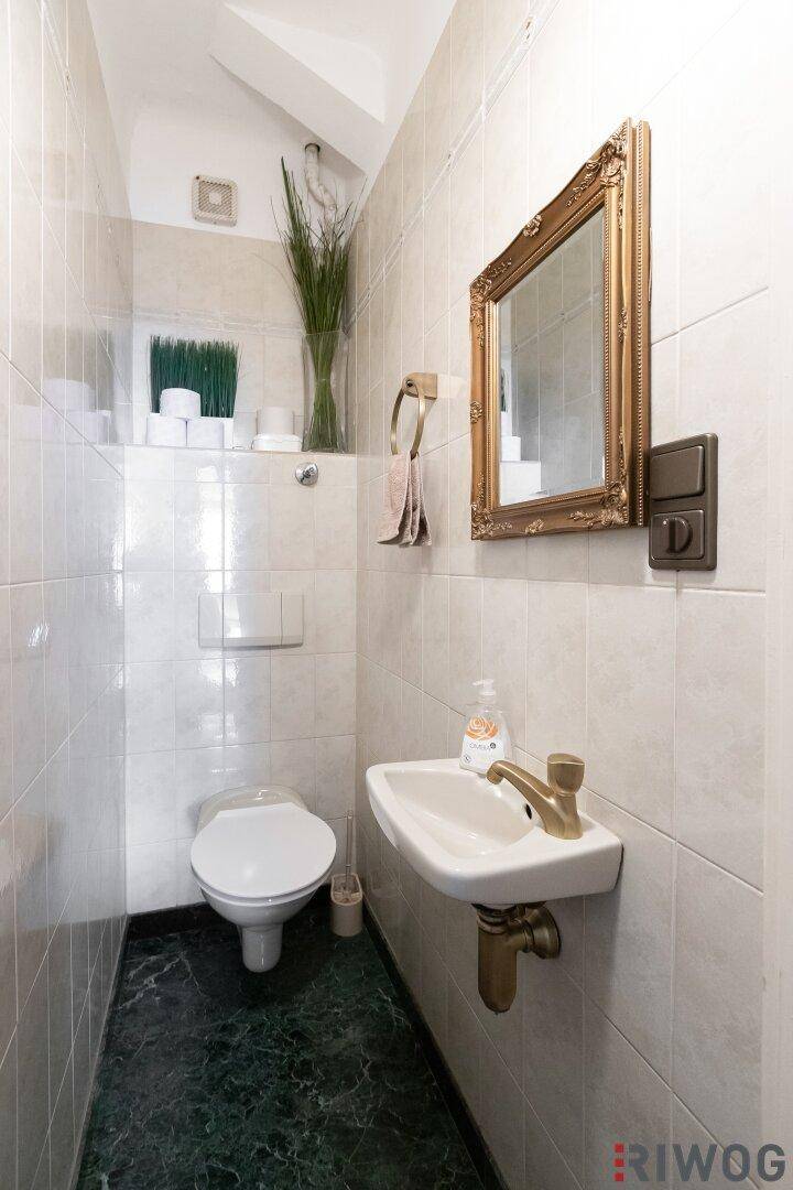 Kleines Gäste-WC mit Waschbecken, Toilette und einem dekorativen goldenen Spiegelrahmen.