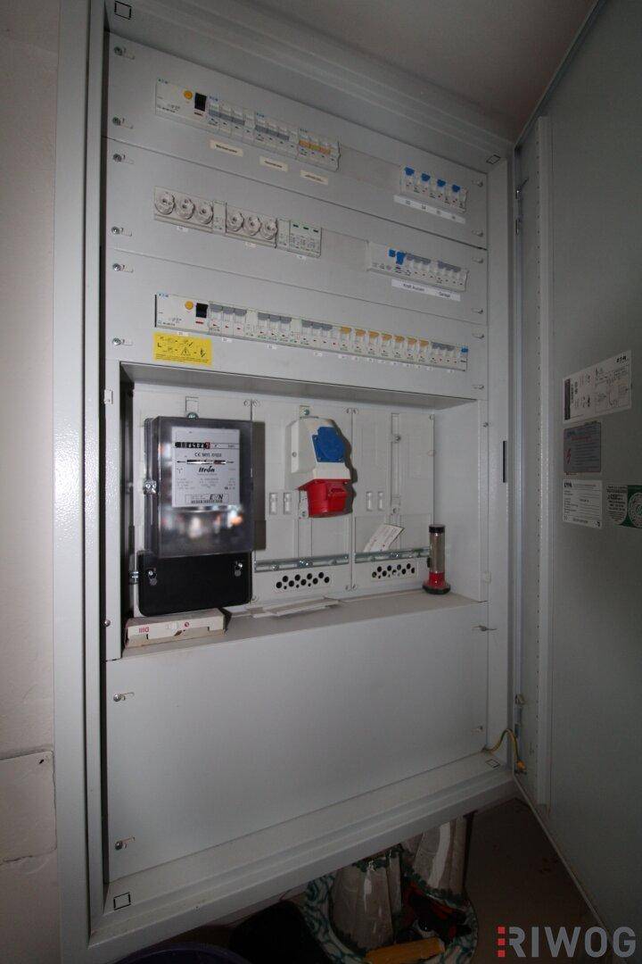 Elektrischer Verteilerkasten mit Zählern und Sicherungen in einem Technikraum.