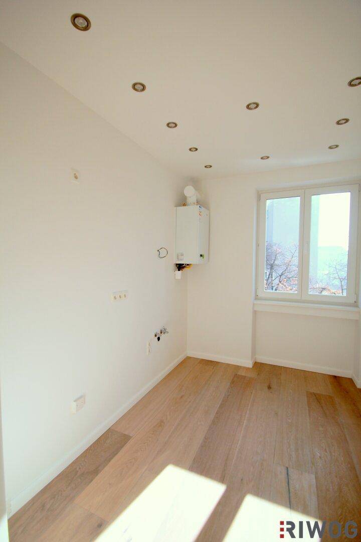 Helles Zimmer mit Holzboden und Fenster, ausgestattet mit einem Warmwasserbereiter an der Wand.