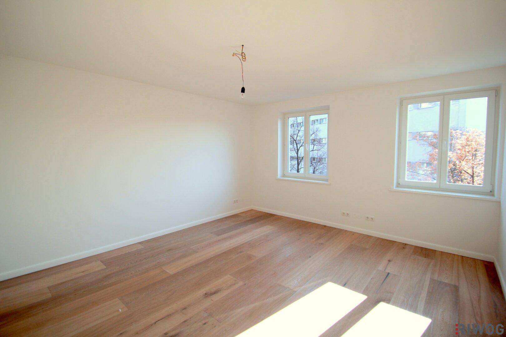 Lichtdurchflutetes Zimmer mit Holzboden und großen Fenstern, ideal als Schlaf- oder Arbeitszimmer.