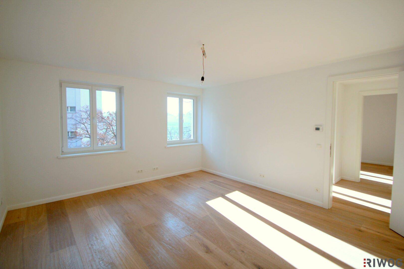 Geräumiges, helles Schlafzimmer mit Holzboden und zwei großen Fenstern, die viel Licht hereinlassen.