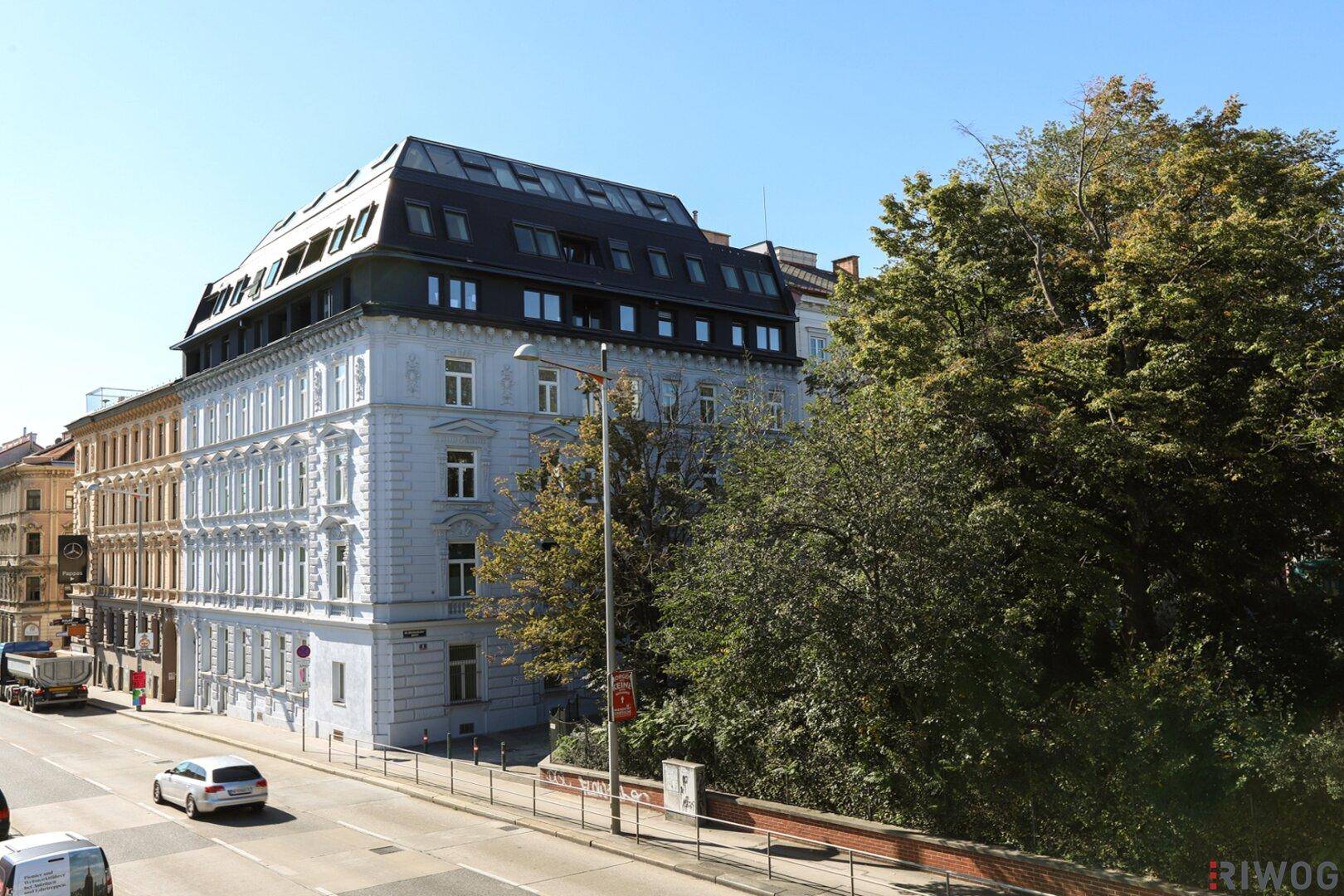 Weitwinkelansicht des sanierten Altbaus mit modernem Dachausbau, angrenzender Straße und grüner Umgebung.