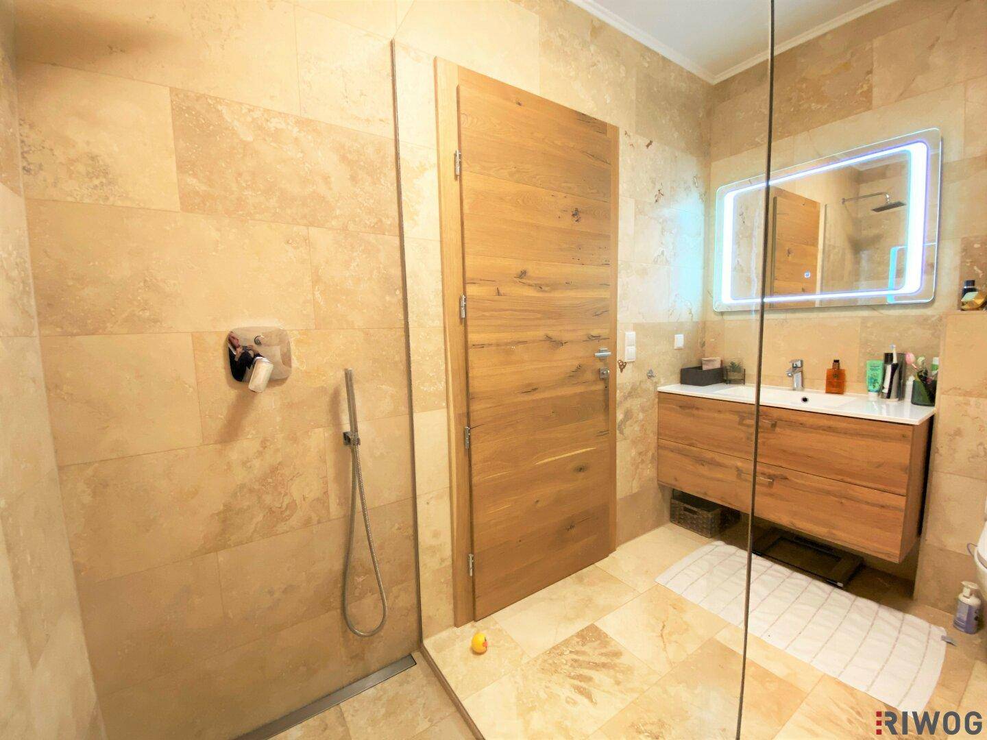 Modernes Badezimmer mit begehbarer Dusche, Einzelwaschbecken und beigefarbenen Natursteinfliesen.