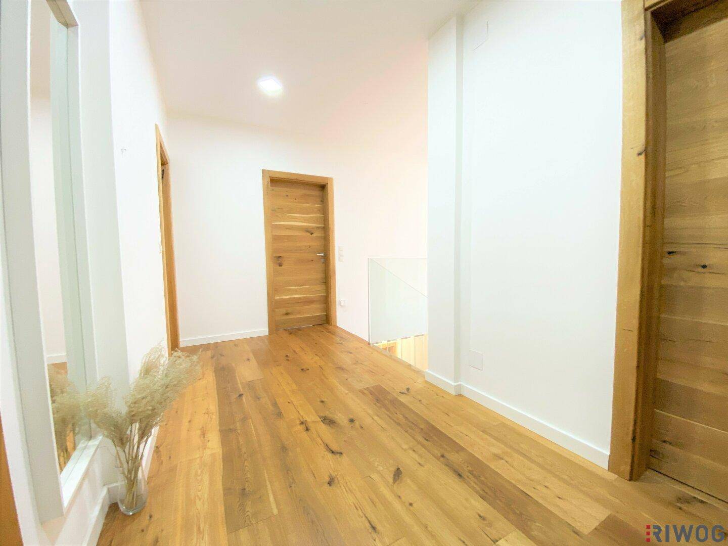 Langer, heller Flur mit warmem Holzboden und modernen Holztüren.