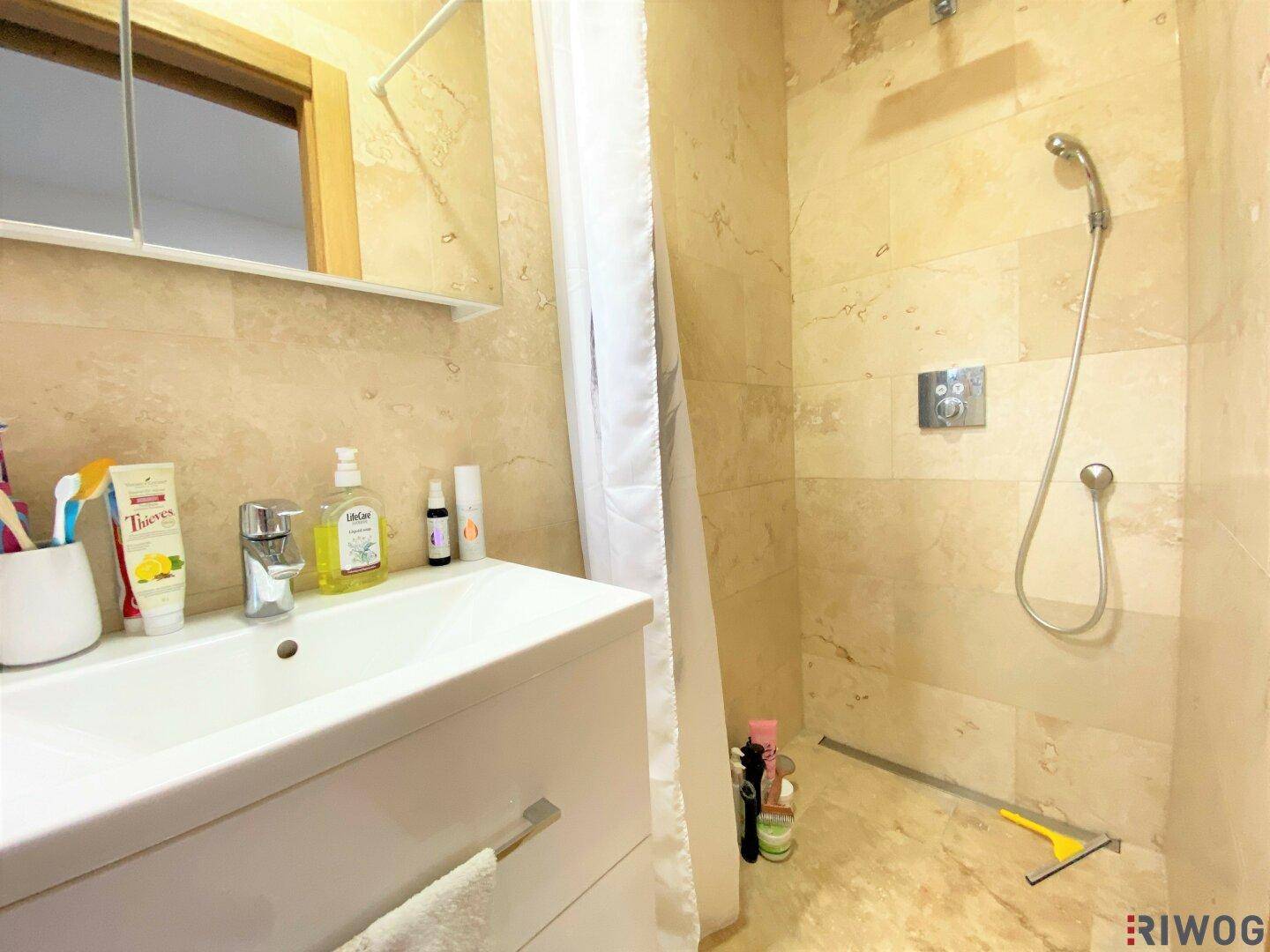 Badezimmer mit Einzelwaschbecken, Spiegelschrank und beigefarbenen Fliesen im Duschbereich.